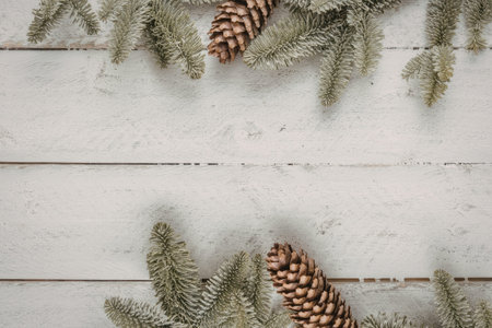 Pine branches and pine cones are arranged on a white wooden background creating a festive christmas...