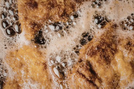 Crispy fried chicken wings being cooked in hot oil with bubbling foam surrounding them in a deep...