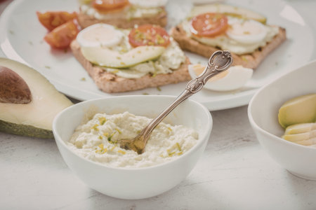 Fresh guacamole in a bowl accompanied by toasted bread topped with avocado, hard boiled egg, and...