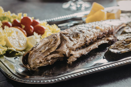 Grilled fish served on a decorative silver platter with a fresh salad of lettuce, tomatoes, and...