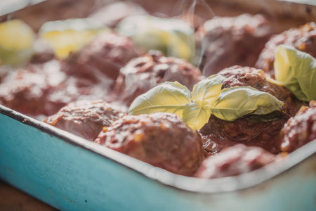 Freshly baked meatballs smothered in rich tomato sauce and topped with fresh basil leaves in a blue...