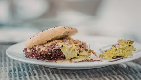 Pulled pork sandwich with coleslaw and mixed greens on a white plate served in a casual restaurant...