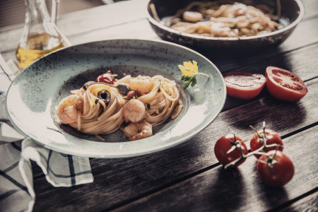Delicious seafood pasta dish served on a wooden table with fresh vegetables and herbs accompanying the meal beautifully, creating a mouthwatering culinary presentation.の写真素材