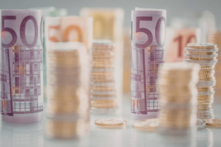 Rolled fifty euro banknotes and stacks of euro coins on a reflective surface symbolizing financial...