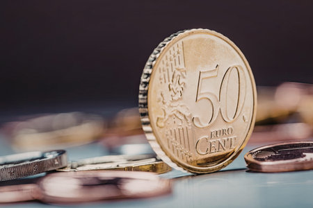 Fifty euro cent coin standing upright surrounded by various other euro coins on a light reflective...