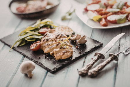 Grilled chicken breast served with mixed vegetables and mushrooms on a slate plate accompanied by a...