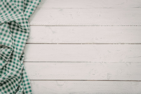 Green and white checkered fabric lies on white painted wooden planks creating a cozy rustic...