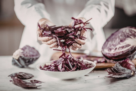 Person in a white shirt prepares fresh red cabbage for cooking by shredding it into a white bowl on...