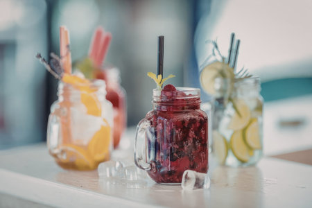 Three mason jars filled with infused water featuring different fruits and herbs sit on a light modern countertop.の写真素材