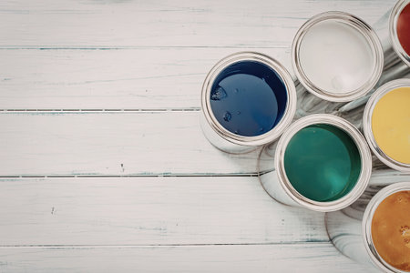 Six vibrant paint cans in different colors rest on a white wooden surface, showcasing a variety of hues for artistic and decorative purposes.
