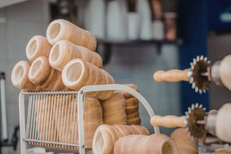 TrdelnÃ­k pastry displayed in a metal basket with wooden rollers and baking equipment visible in...