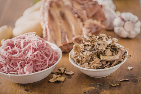 Bowls of sauerkraut and dried mushrooms sit on a rustic wooden table surrounded by cured meat and...