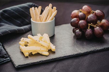 Cheese sticks, breadsticks, and grapes arranged on a slate platter, making for a simple yet...