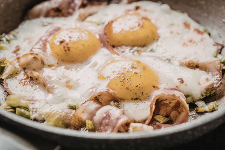 Freshly cooked sunny-side-up eggs with savory bacon and vibrant green vegetables sizzle deliciously in a hot pan, perfect for a hearty breakfast or brunch.の写真素材