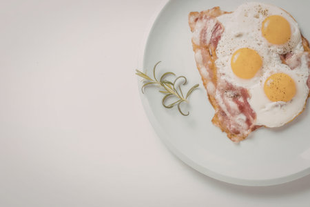 Eggs benedict with crispy bacon and fresh rosemary served on a white plate for a delicious and...