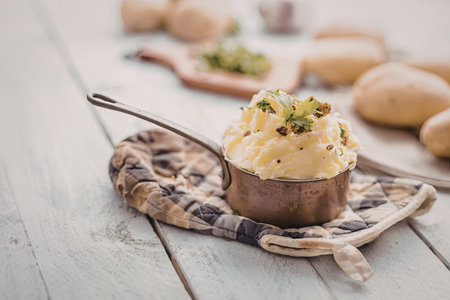 Mashed potatoes served in a copper saucepan garnished with fresh herbs and crispy bits on a rustic wooden table.の写真素材