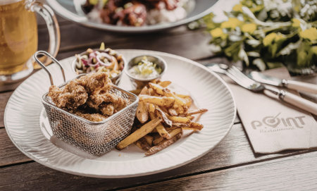 Crispy fried chicken and sweet potato fries served with dips on a white plate accompanied by a glass of beer on a wooden table.の写真素材