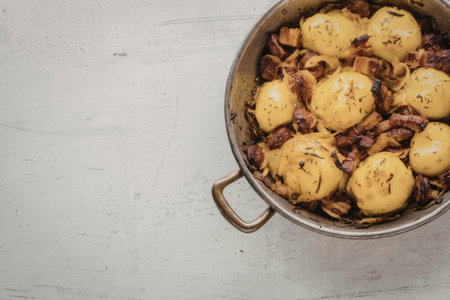 Pan seared potatoes with crispy bacon and herbs cooked in a metal pan on a white textured background...