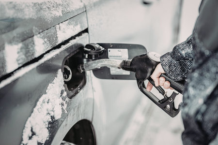 Person is refueling a car with gasoline on a snowy day, with frost visible on the vehicle and ground...
