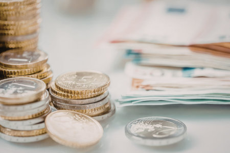 Stacks of euro coins and banknotes are neatly arranged on a white surface for financial transactions...