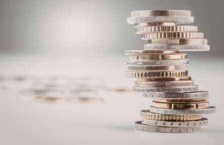 Stack of coins arranged in a precarious balance on a white surface with additional coins blurred in...