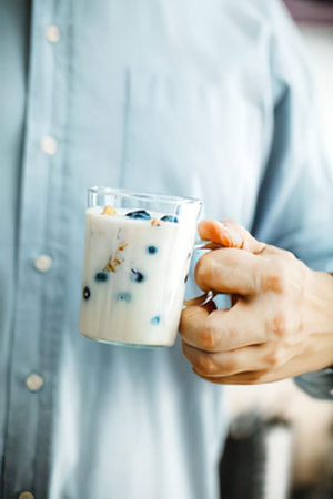 a person wearing a blue shirt holding a glass of yogurt with blueberries and granola