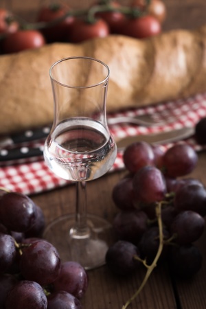 Glass of Grappa with Grape, Bread and Tomatoes on a wooden Tableの写真素材