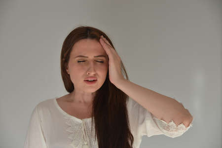 Girl is suffering headache in front of gray backgroumdの写真素材