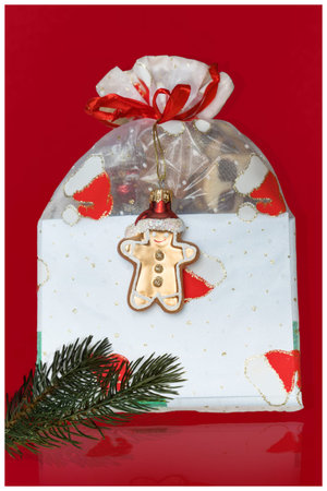 Christmas gift box with gingerbread cookie and fir branch on red background