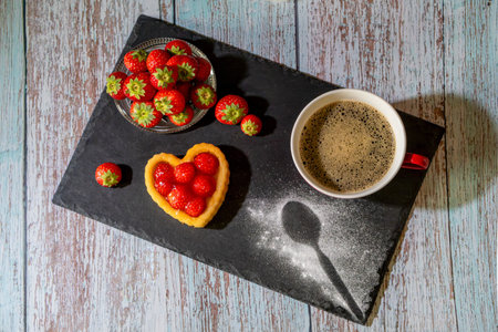 Cup of coffee with strawberries and heart shaped cake on wooden tableの写真素材
