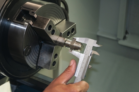 Worker measuring threaded part with caliper inside a CNC machineの写真素材