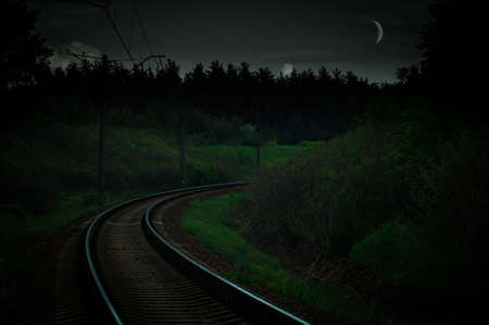 Railroad turn at twilight at moonlight with forest in the backgroundの写真素材