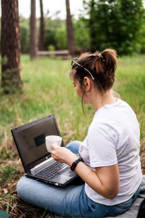 Girl freelancer works on a computer in the bosom of nature with a cup of coffeeの写真素材