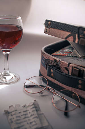 Still life with a travel case, round glasses, a note with a handwritten text, a glass of red wineの写真素材