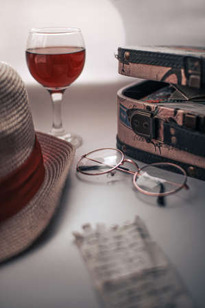 Still life with a travel case, round glasses, a note with a handwritten text, a glass of red wine and a hatの写真素材
