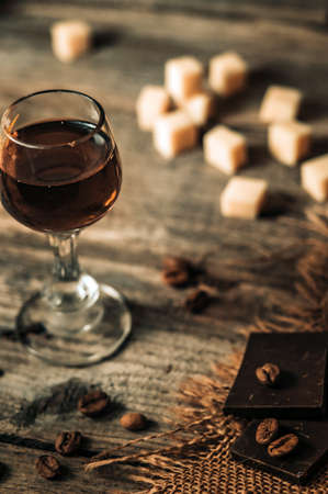 Still life with a glass of cognac, pieces of cheese, chocolate and coffee beans on a wooden backgroundの写真素材
