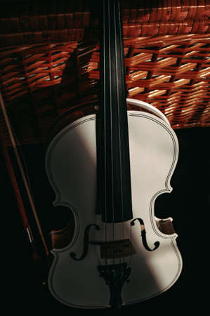 Snow-white violin against the background of a wicker chest with deep shadowsの写真素材