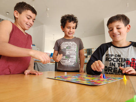 Group of happy children playing board game at table in living room at home