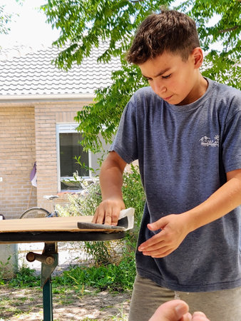 Boy sanding a wooden board with a sand paper in the backyard of his houseの写真素材