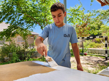 Young boy paints a wooden table with a brush in the garden.の写真素材