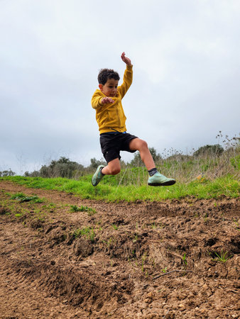 Boy jumping on a hill in the countryside, wearing a yellow shirt
