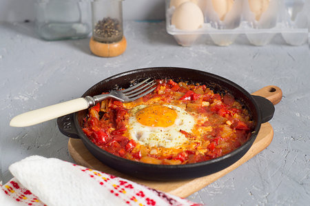 Traditional Oriental dish of shakshuka eggs in a dark pan on a gray background .