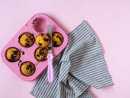 Muffins in a pink cupcake shape, a kitchen spatula with a pink handle, a gray striped towel on a pink background. Flat lay. Top view.の写真素材