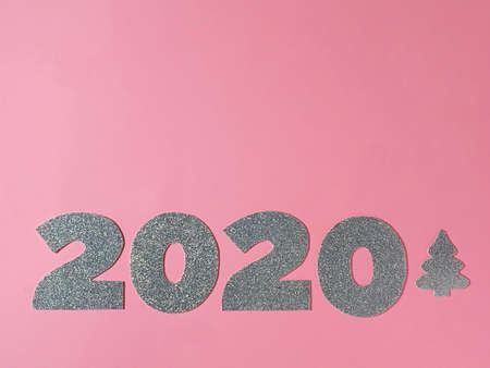 Celebrating the new year 2020. Silver mother-of-pearl paper, number 2020 with a Christmas tree on a pink background. Flat lay.の写真素材