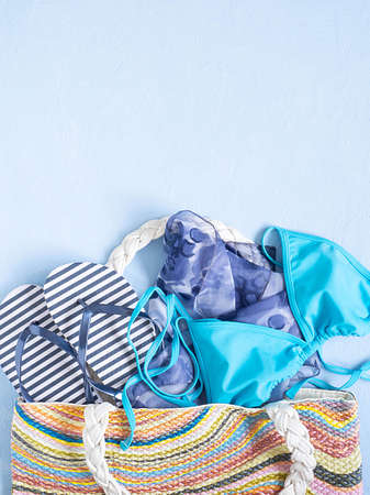 Summer beach bag with elegant women's accessories on a blue background. Top view beach bag with swimsuit, flip flops, headscarf . Flat lay the material. Summer fashion, leisure conceptの写真素材