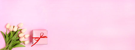 Bouquet of pink tulips and a gift on a pink background. Banner.