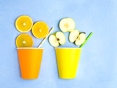 Orange and Apple slices, paper cups on a blue background. Fresh juice concept. Natural and organic...