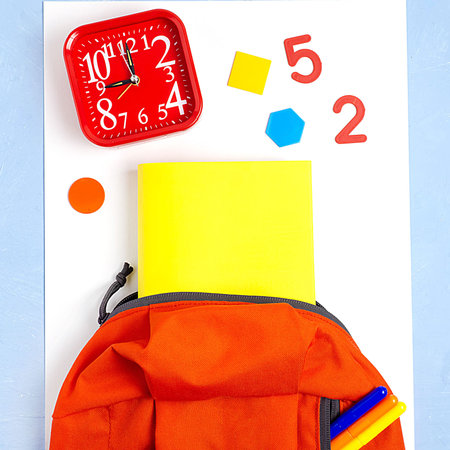 Orange backpack with school supplies on a blue concrete background. The concept of the school.