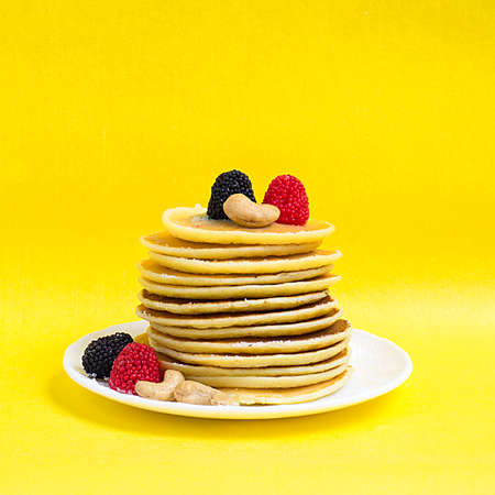 Stack of pancakes with powdered sugar and berries on a yellow background. Copy space.の写真素材