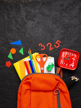 Orange backpack with school supplies on a black concrete background. The concept of the school. Copy...